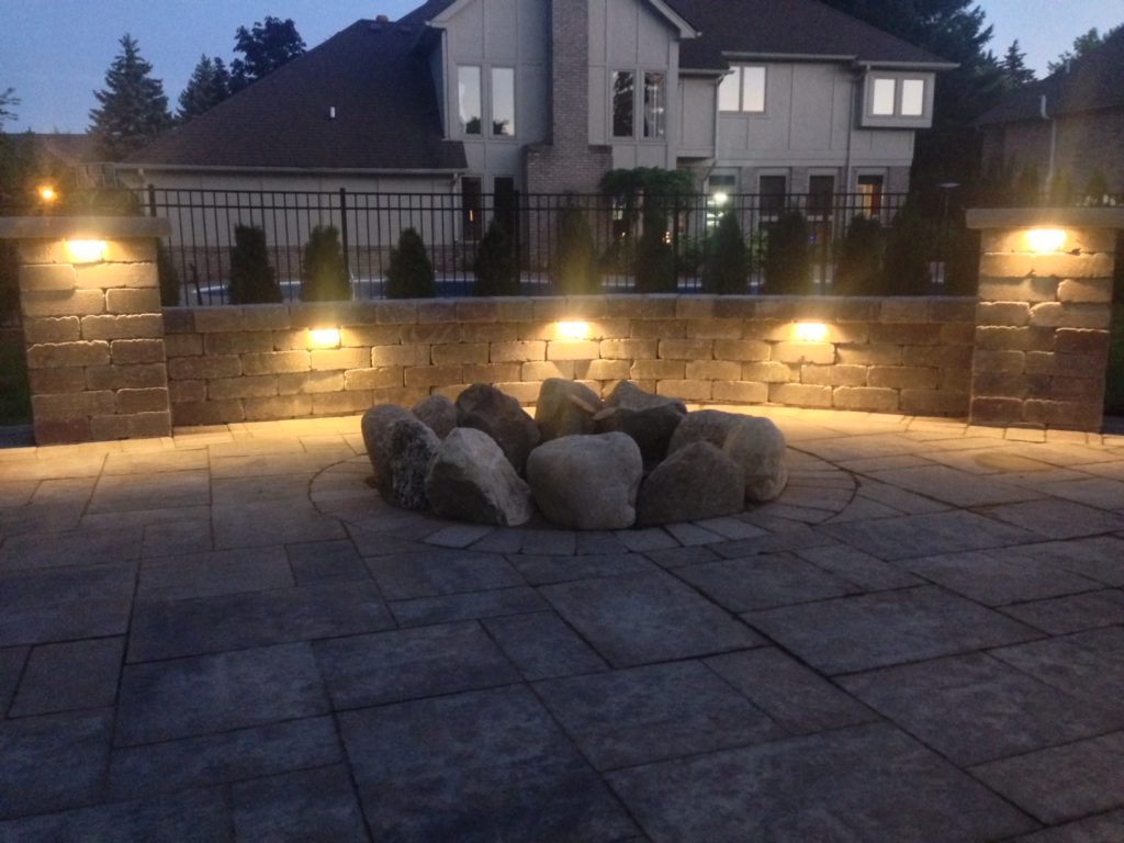 Landscape lighting illuminating a stone patio with a fire pit