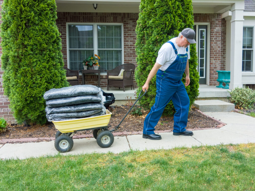 A man pulls several bags of mulch with a wheelbarrow